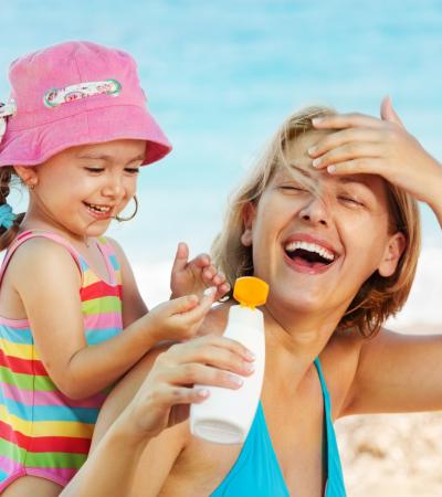 Madre e figlia sorridenti applicano crema solare in spiaggia.